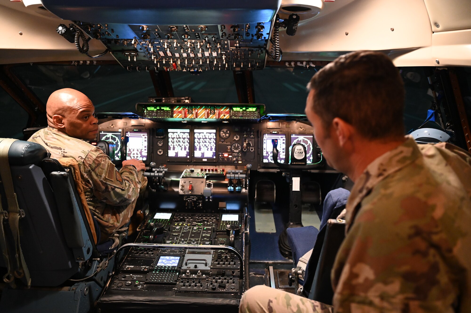 Chief Master Sgt. Travon Dennis (left), 4th Air Force command chief, sits in the left seat of a C-5M Super Galaxy simulator during a tour of the 733rd Training Squadron at Joint Base San Antonio-Lackland, Texas, Aug. 3, 2024.