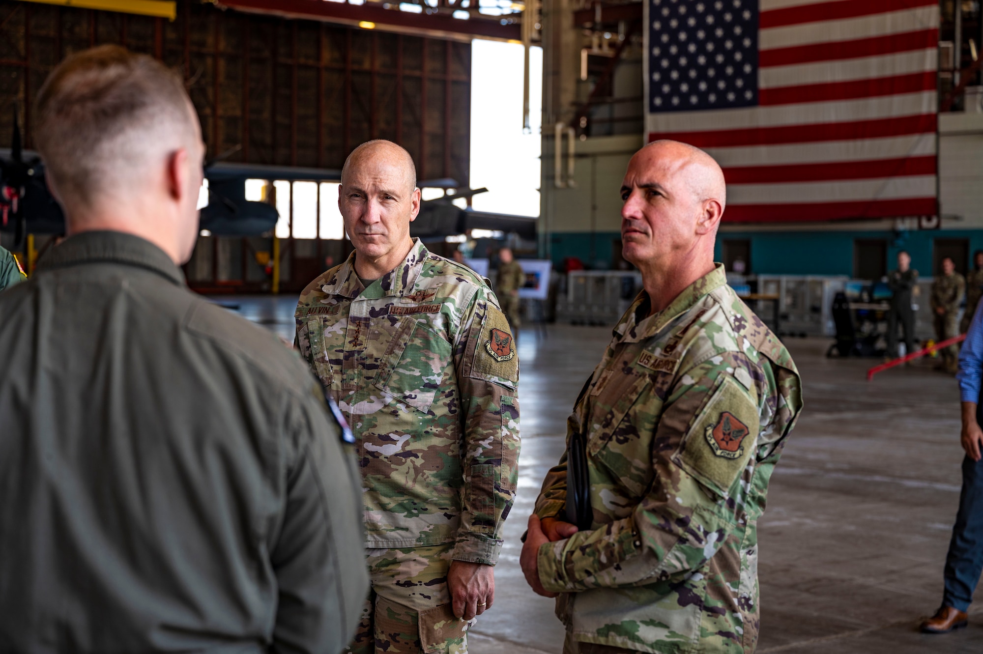 Two men stand looking towards another person.