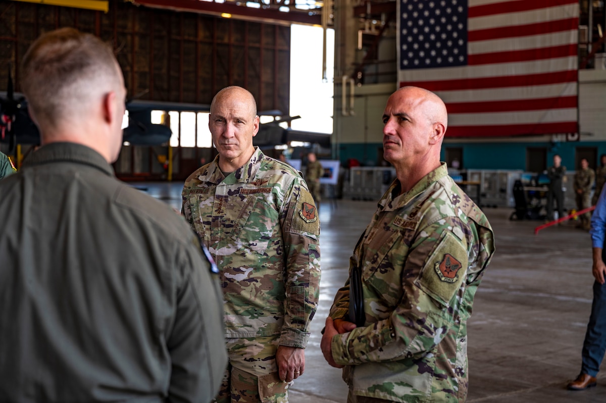 Two men stand looking towards another person.
