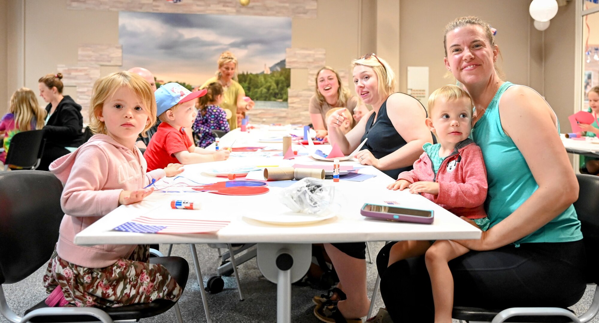 Mothers and children smile at a camera at a craft event.