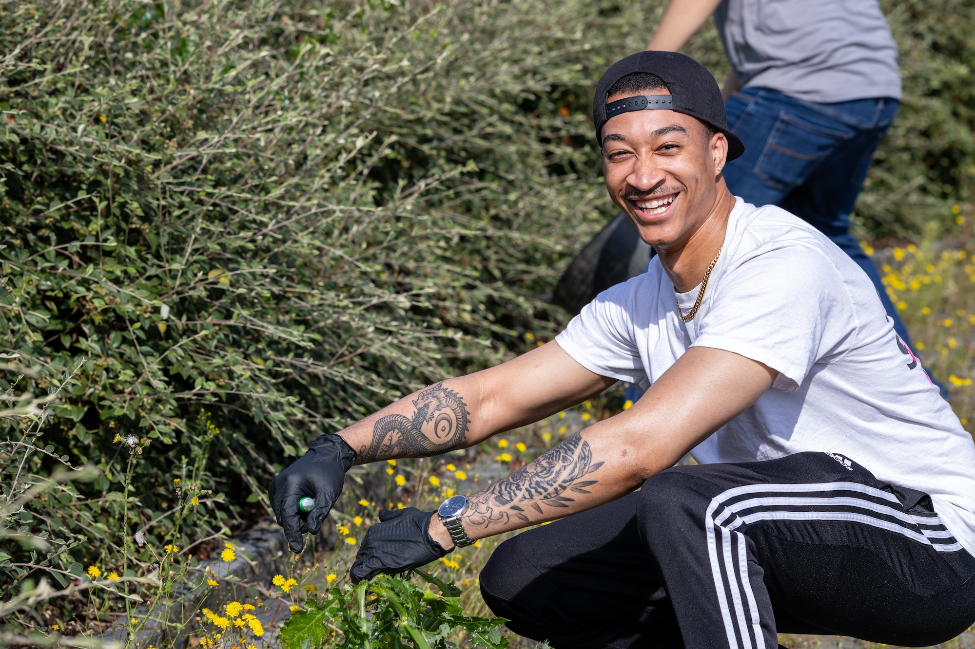 Student smiles and pulls weeds for an Airman Leadership School community service project