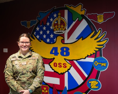 U.S. Air Force member poses in front of the 48th Operational Support Squadron logo.