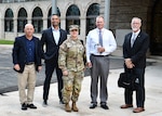 Five people are posed standing and facing the camera in front of a building, in the center is Army Col. Michelle Agpalza