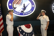 Cmdr. Christopher Tilley (right) Commanding Officer for Strategic Systems Programs (SSP) Project Management Office for Flight Systems (SPF) relieves Capt. Michael Woehrman (left), SPF's former commanding officer, with a salute during a change of command ceremony Thursday. Both officers are standing in front of each other saluting. They are wearing summer white dress uniforms and standing in front of the SPF emblem. Cmdr. Christopher Tilley was the former Weapons Officer at Strategic Weapons Facility Pacific and assumed command at SPF during the ceremony which marks longstanding tradition of passing leadership responsibilities in the Navy. SPF—one of SSP’s many field sites—provides the technical oversight and fleet support for the nation's sea-based strategic deterrent and equip the nation’s Warfighting Navy with safe, secure, reliable, and effective weapon systems (U.S. Navy Photo by Yeoman Submarine 2nd Class Alakai Merino/Released).