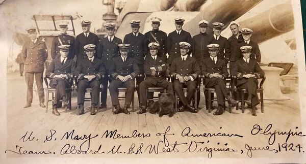 Two rows of men in uniform, one seated and one standing, with the deck of the battleship visible.