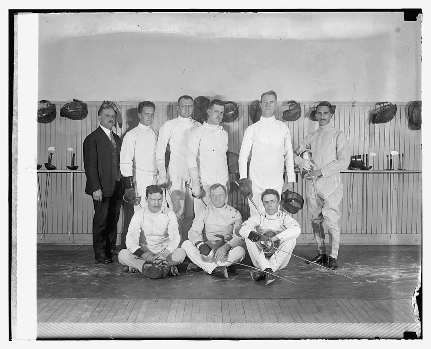 Nine men in a group wearing traditional white fencing uniforms.