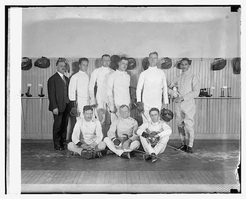 Nine men in a group wearing traditional white fencing uniforms.