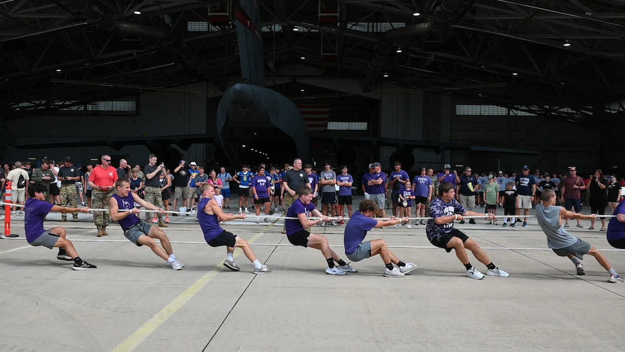 kids pull on a rope in front of an aircraft hangar