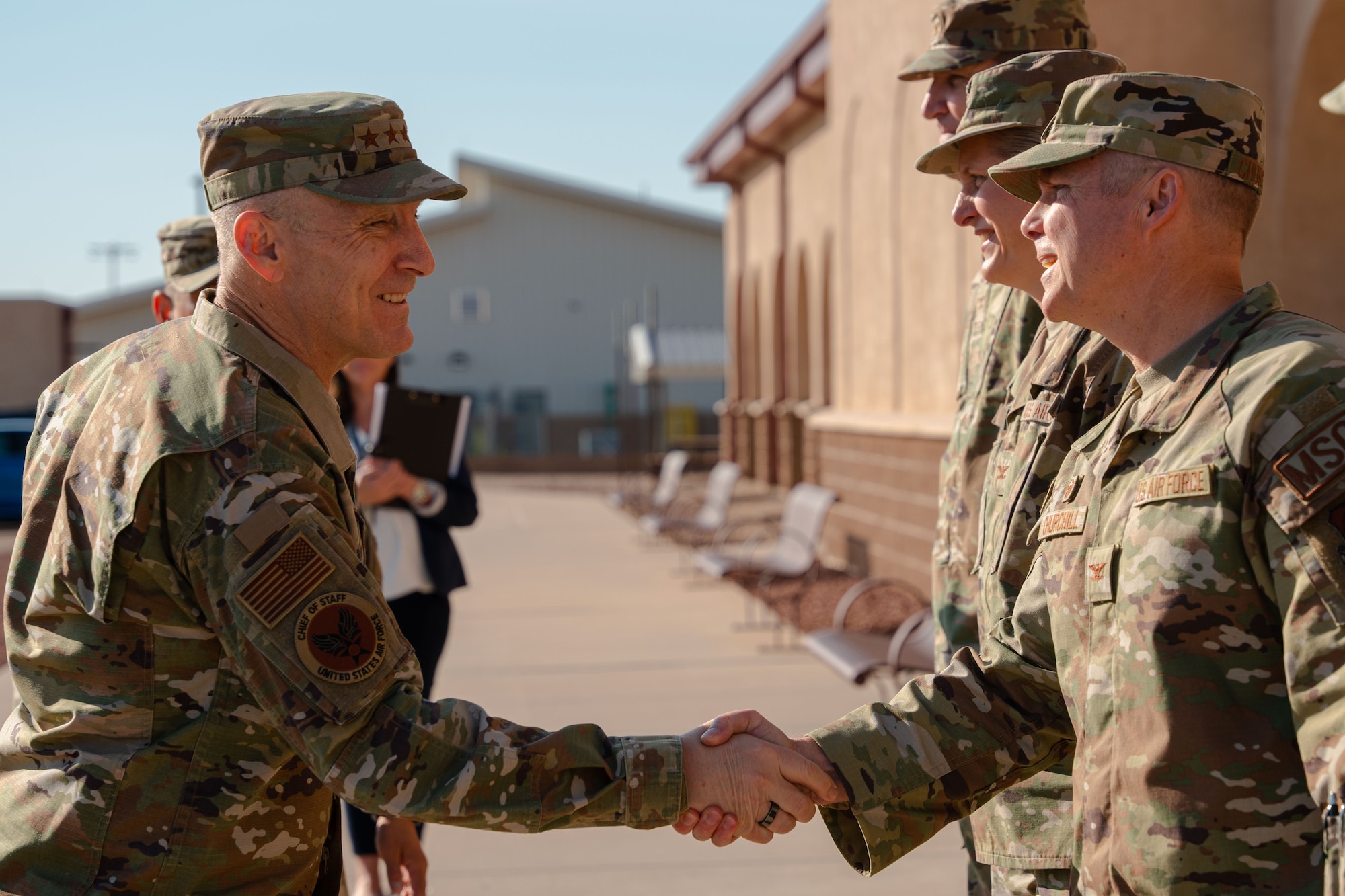 A man in military uniform shakes the hand of another man in military uniform, who is standing in a small line of men in military uniform.