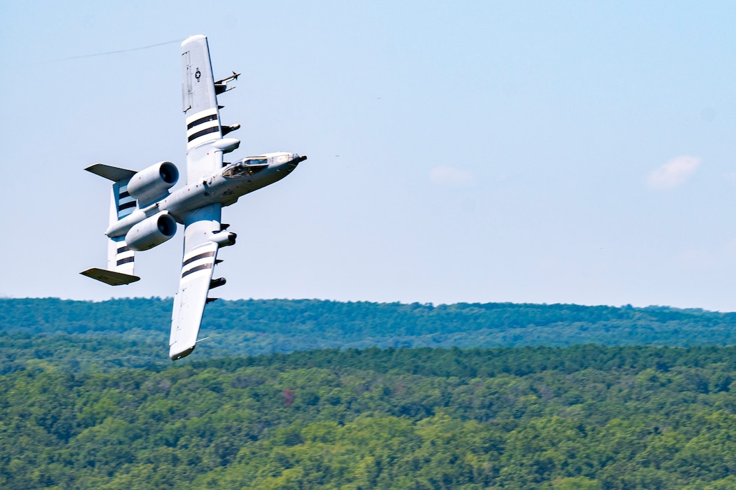 An A-10 banks over a forest.