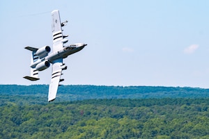 An A-10 banks over a forest.