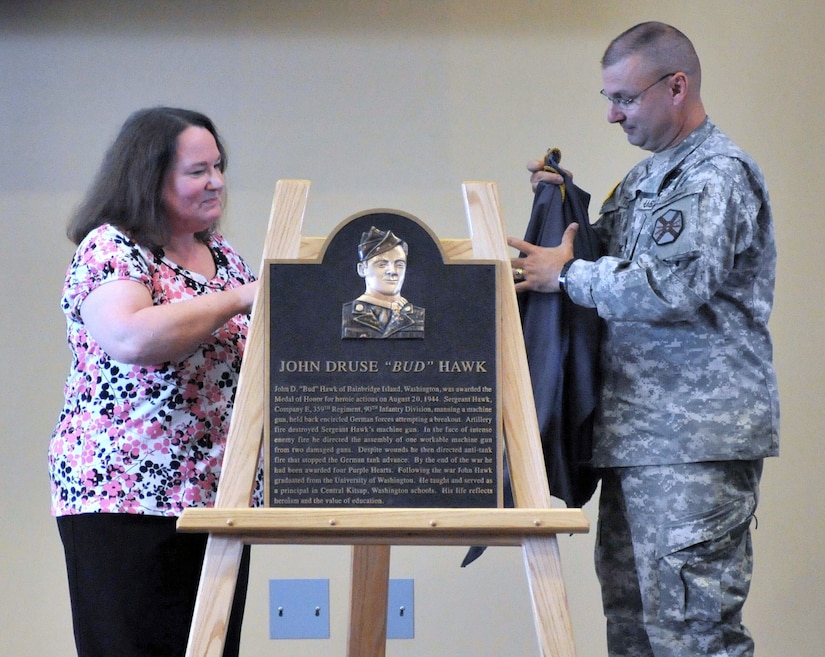 Two people unveil a plaque that sits on an easel.