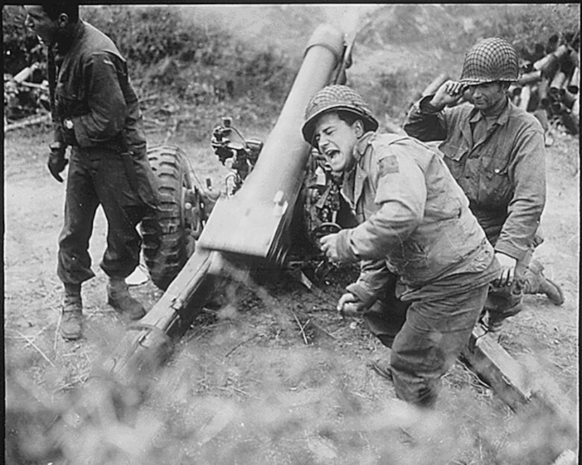 Three men fire a howitzer gun.