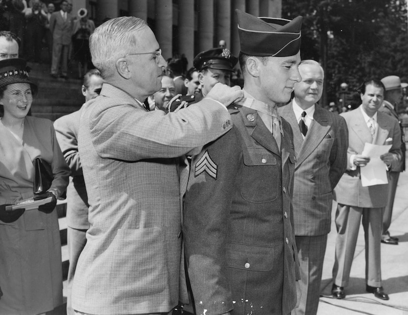 A man places a medal around another man’s neck as others watch.