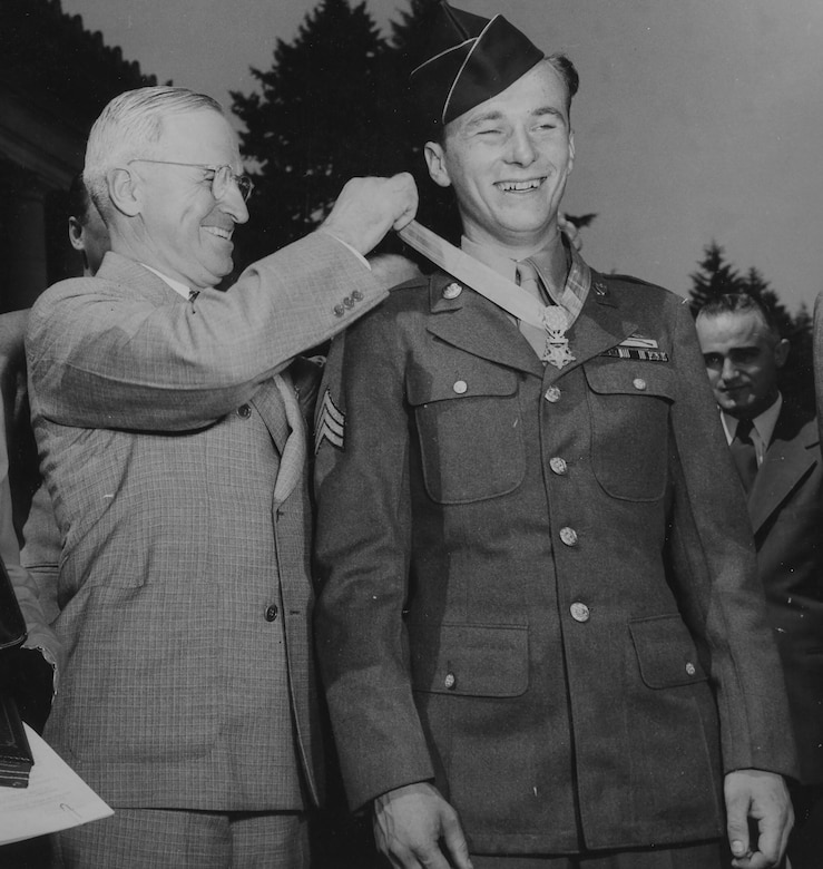 A man places a medal around another man’s neck as others watch.