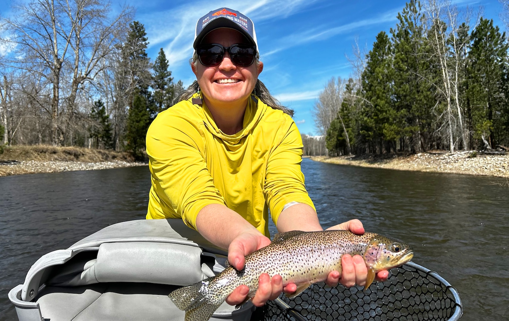 A picture of Sue Kerver out on the water in a yellow shirt with a fish and a net.