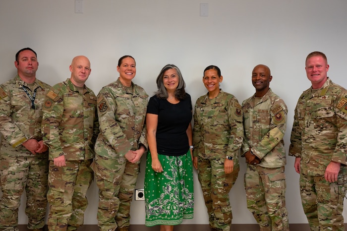 A woman in a black shirt and green skirt poses for a photograph with a group of men and women in military uniform.