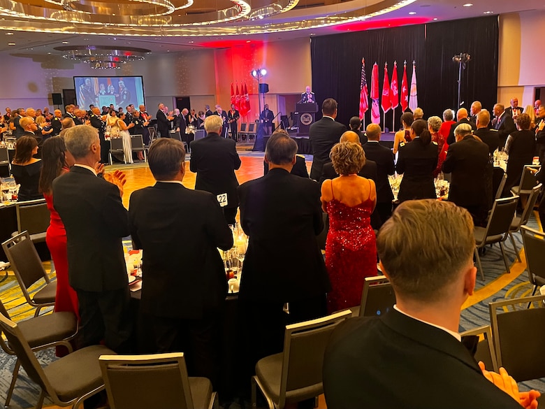 a group of individuals in a large ball room stand and applaud.