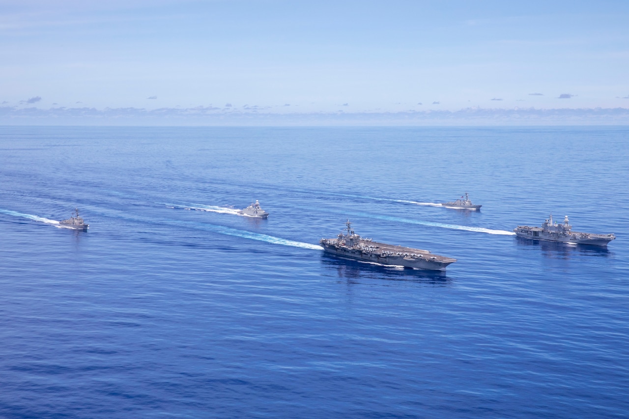 An aerial view of five large naval vessels sailing on the ocean.