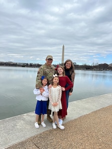 A family poses for a group photo with the Washington Monument behind them.
