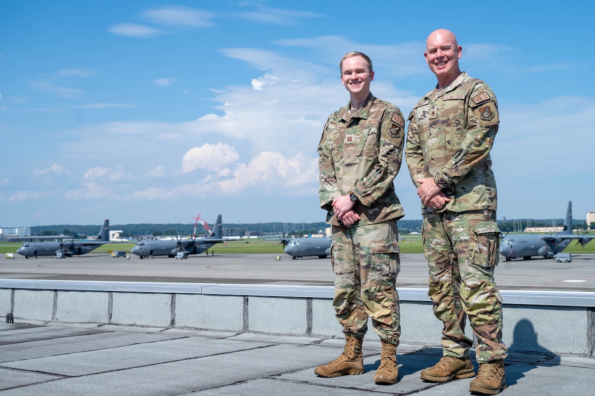 Two service members pose for a photo in front of planes.