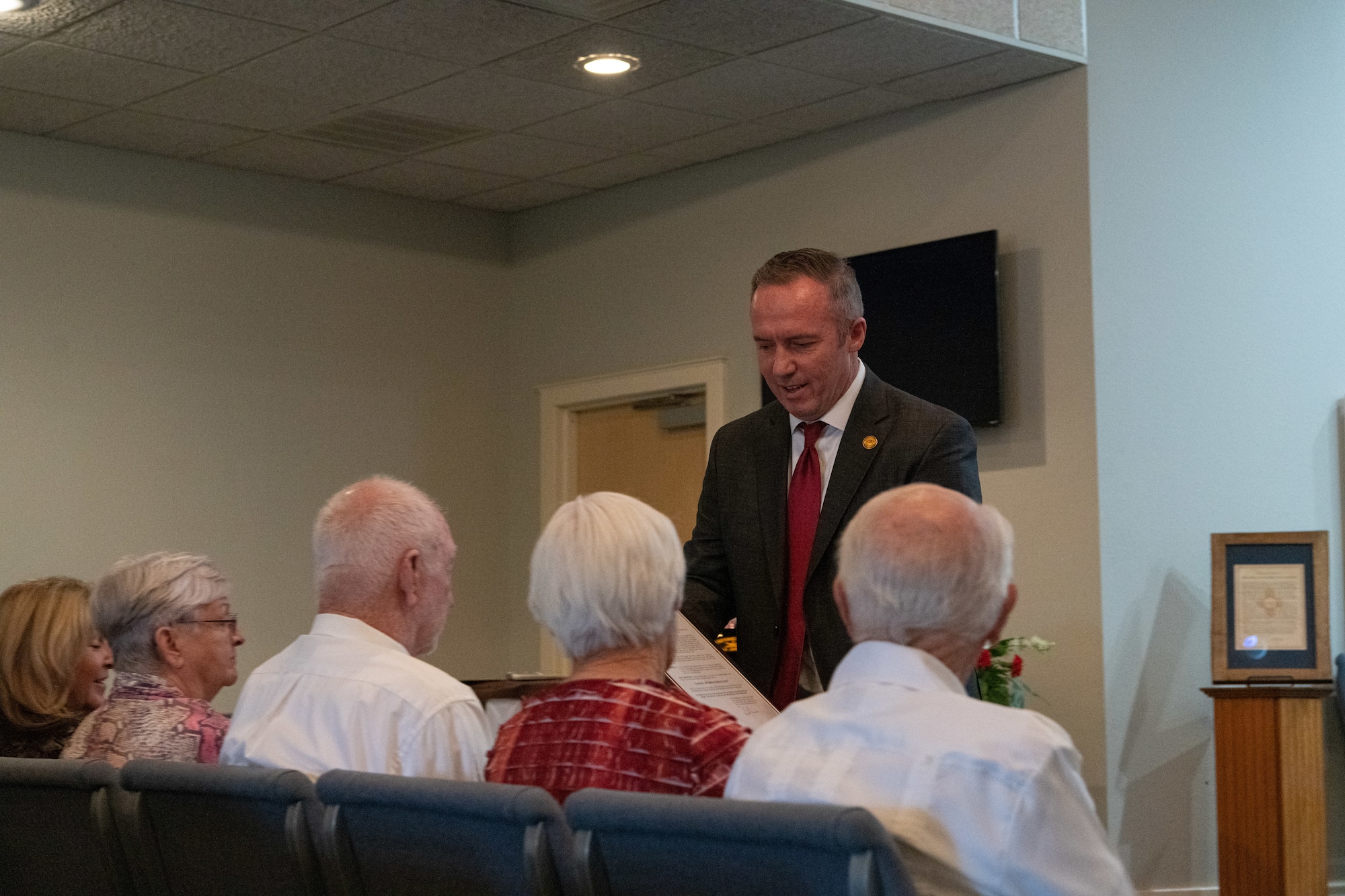A man in a suit presents a gift to several seated elderly individuals.