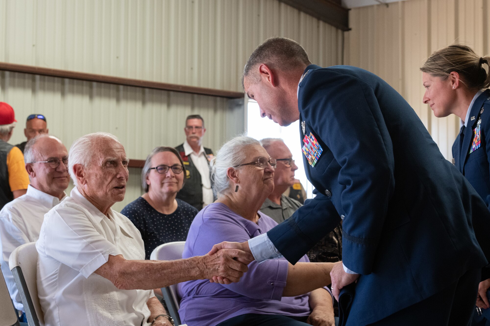 A man and woman in military uniform stand while shaking hands with an elderly man and woman who are seated.