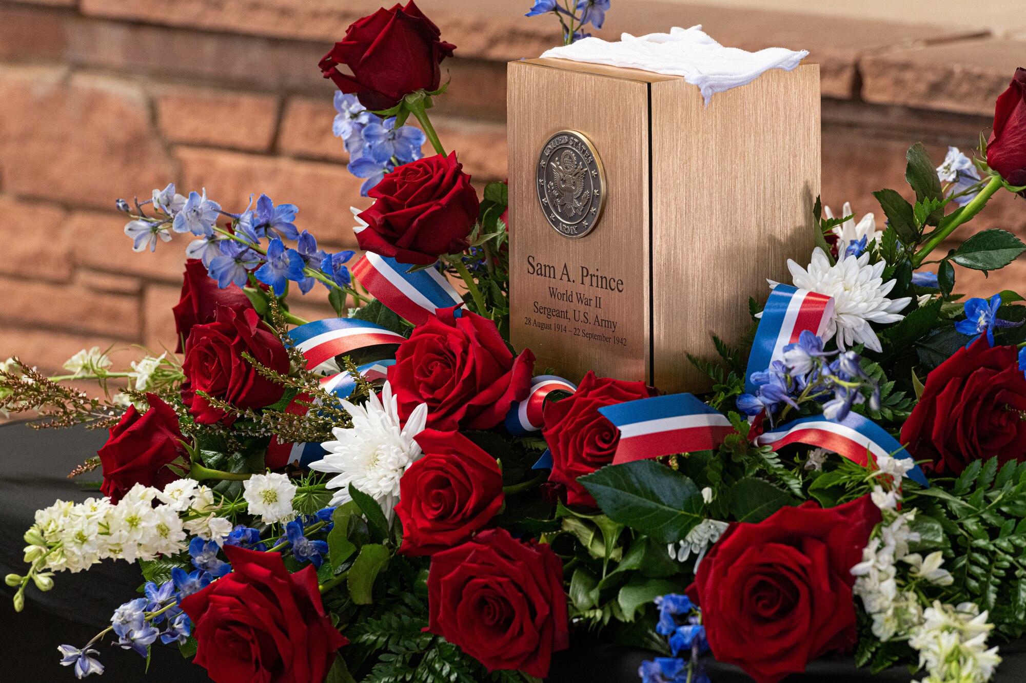 A wooden box of remains sits on a bouquet of flowers on display at a funeral.