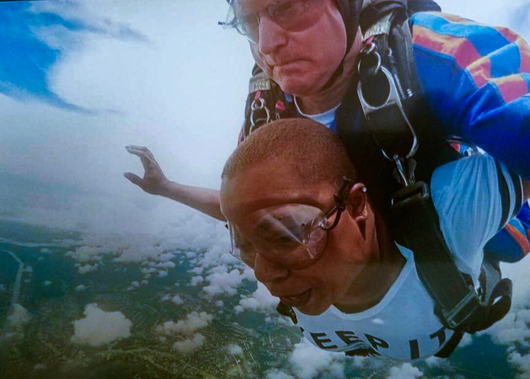 A man and a woman are skydiving together by being strapped together with the woman on top. both are wearing goggles and are above the clouds.