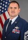 Chief Master Sgt in Air Force dress uniform posing for a photo in front of an American flag.