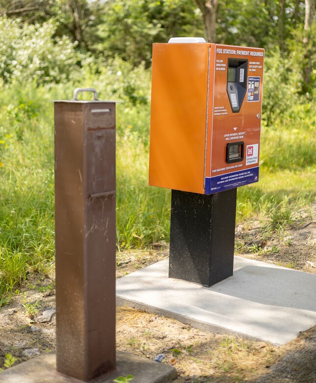 A brown vault stands next to an orange machine with greenery in the background.