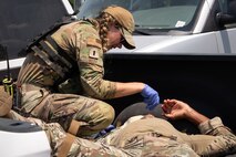 An Airmen with latex gloves and body armor is bent over providing first aid to another Airmen laying in the back of a truck bed.