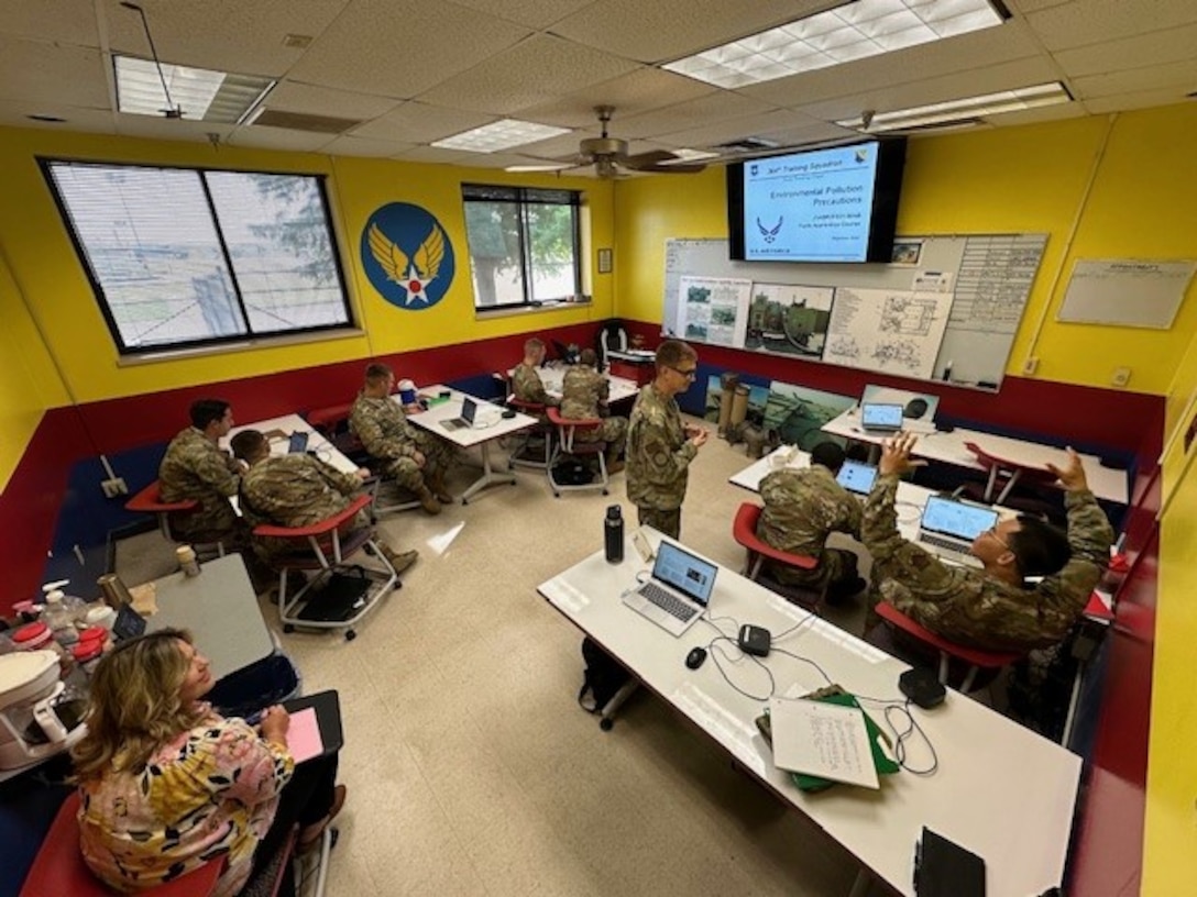 A woman watches a group of Airmen in a classroom.