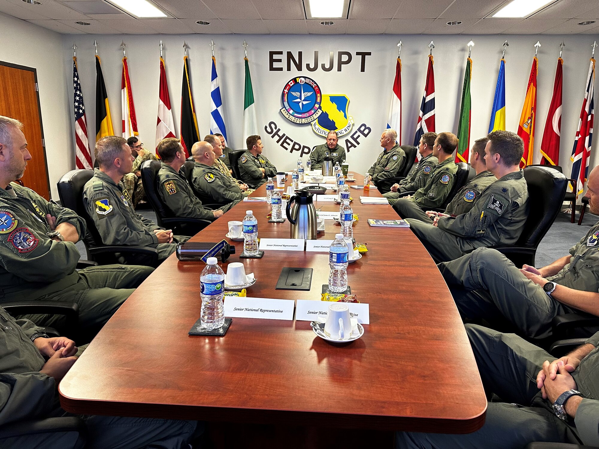 A group of men in flight suits sit around a conference table.