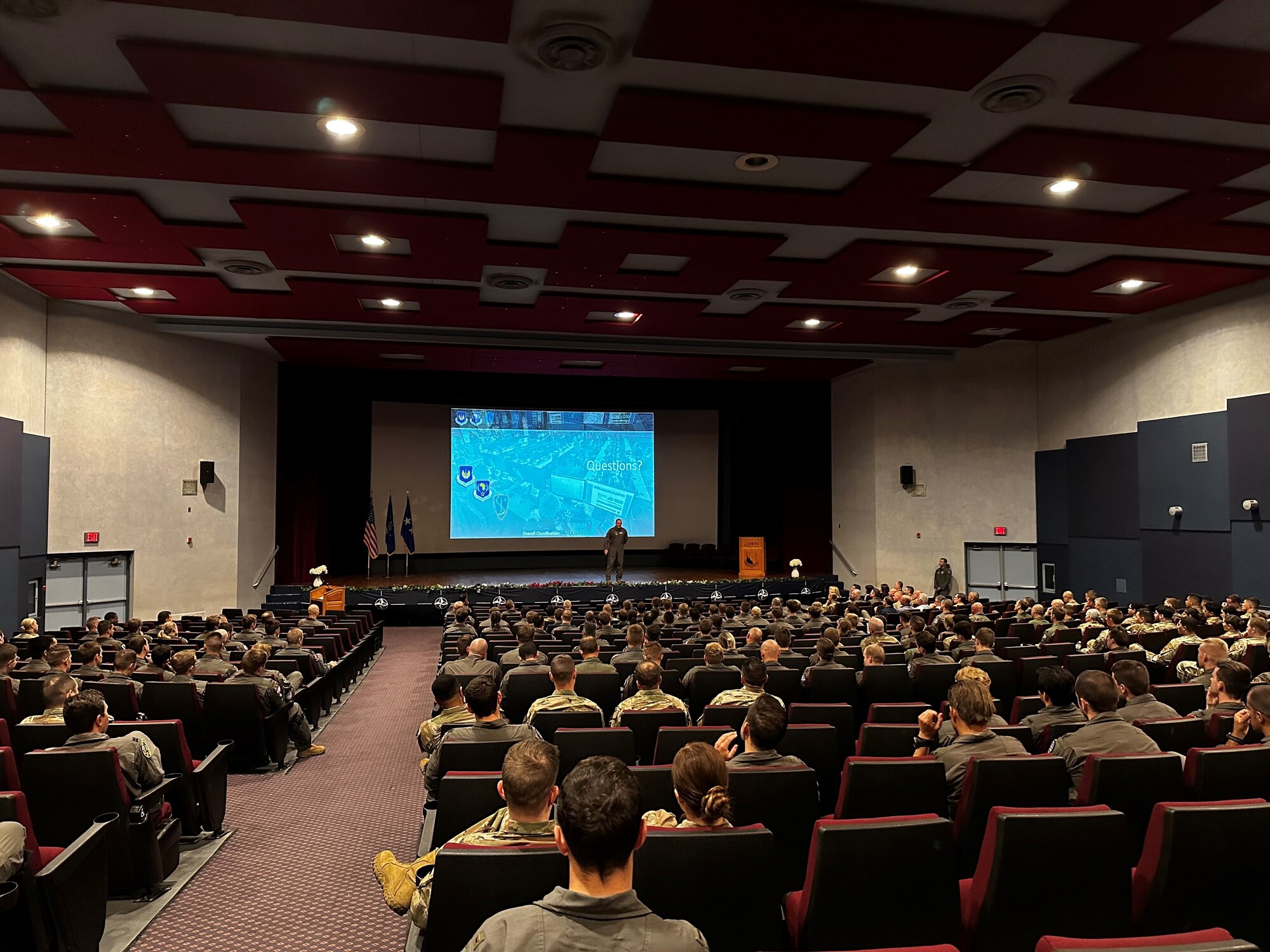 An auditorium full of people with a speaker in front on a stage.