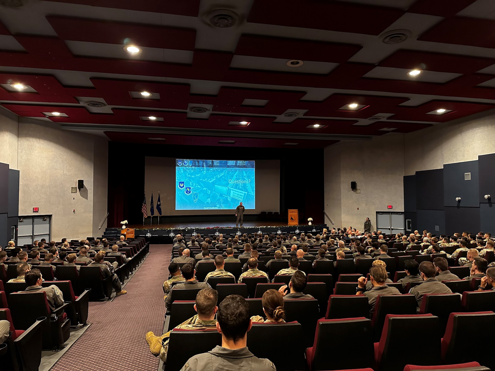 An auditorium full of people with a speaker in front on a stage.