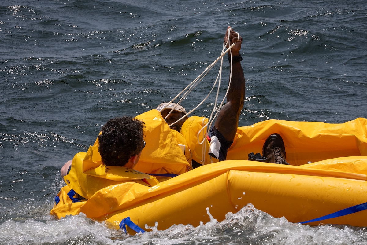 Two men in a raft struggle with ropes while they are battered by rough waves