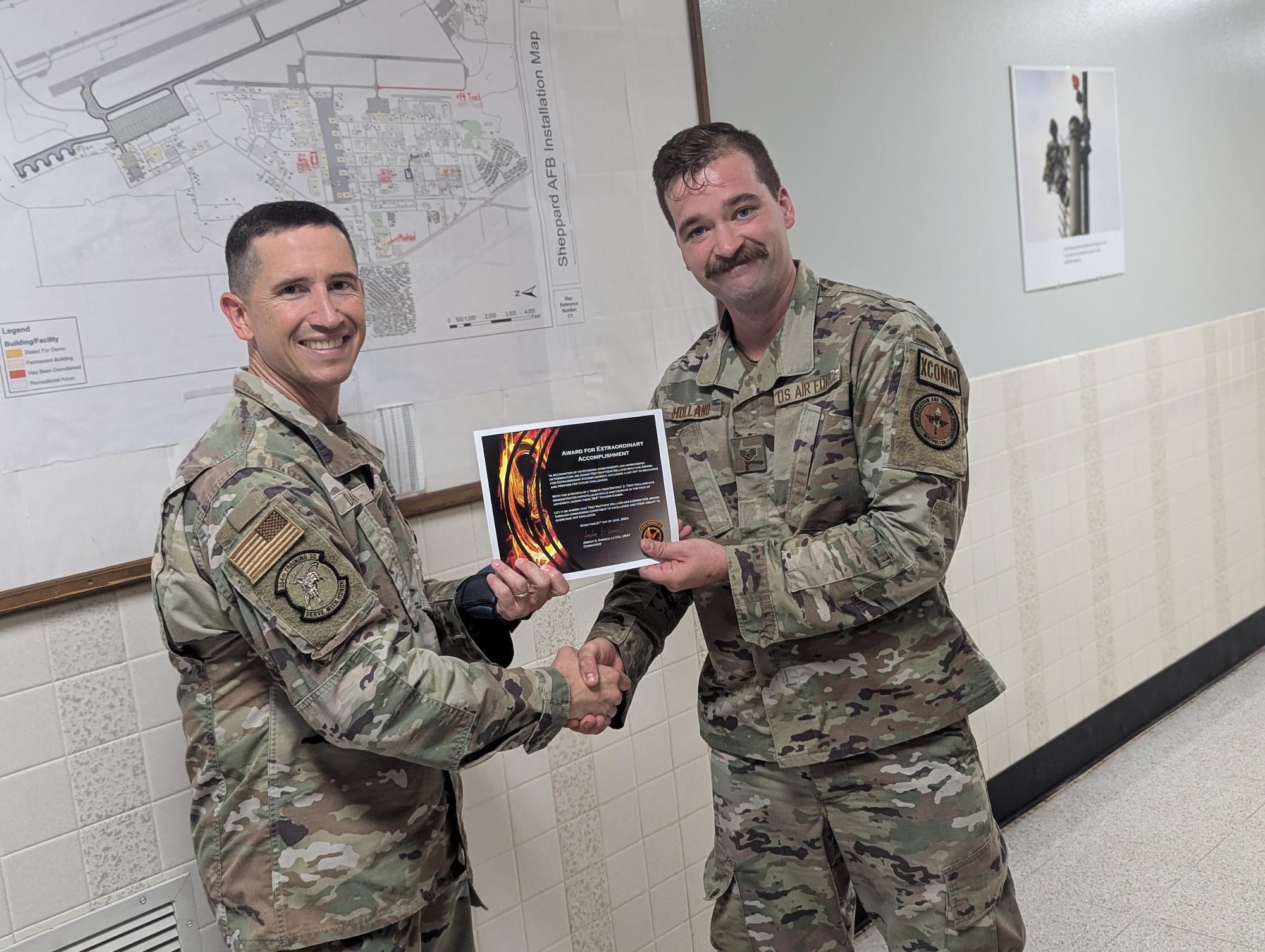 A man in uniform hands another man in uniform a certificate as they shake hands.