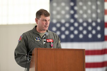 Lt. Col. Lawrence “Mongo” Dietrich stands at a podium with a U.S. flag in the background.