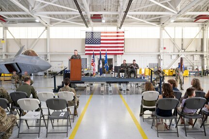 View of audience and stage in a hangar with F-22 Raptor in the left background.