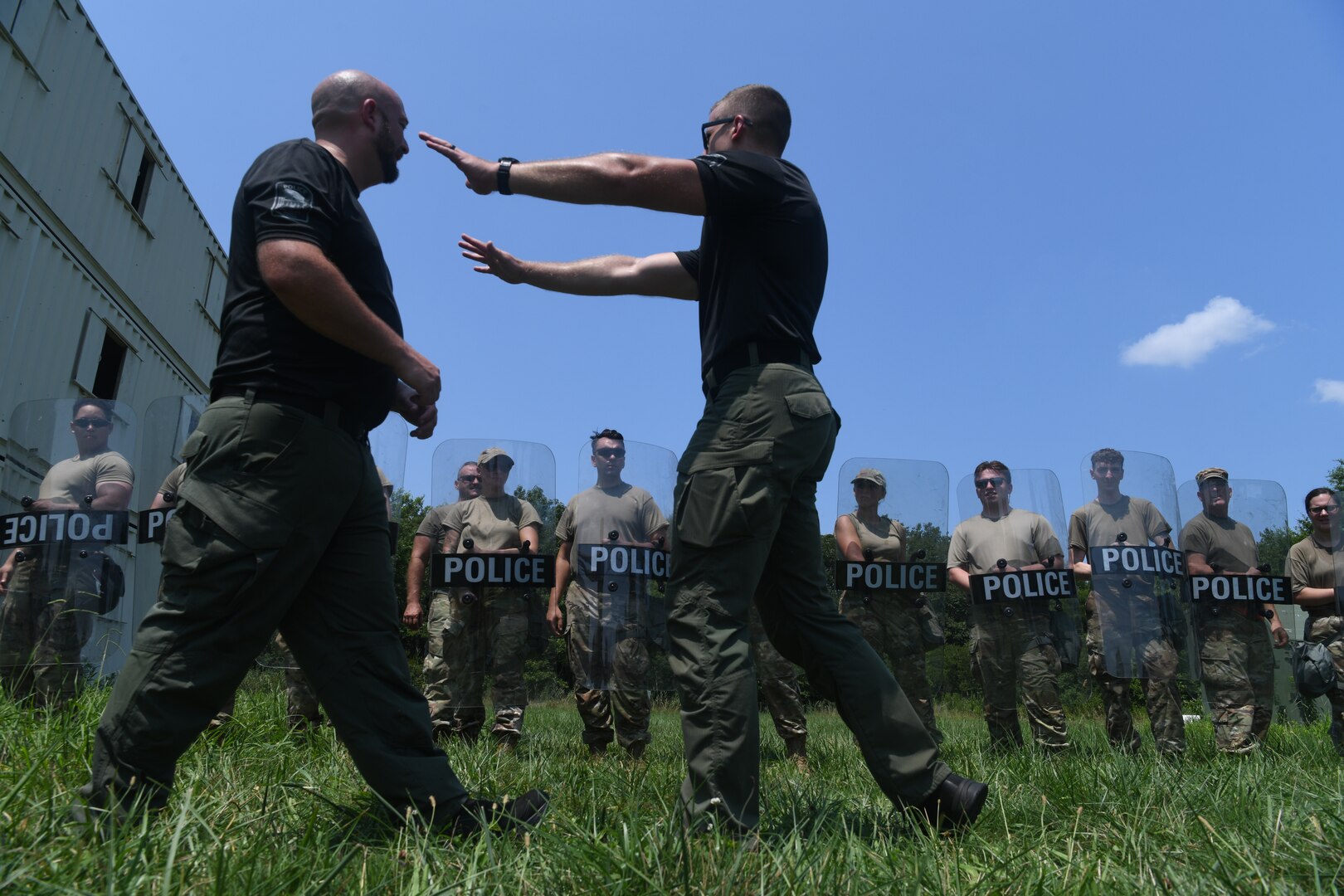 Two police officers demonstrating techniques to line of Airmen behind them.