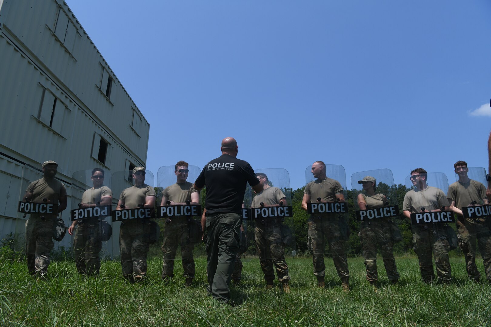 Police officer demonstrating techniques to a line of Airmen holding police shields.