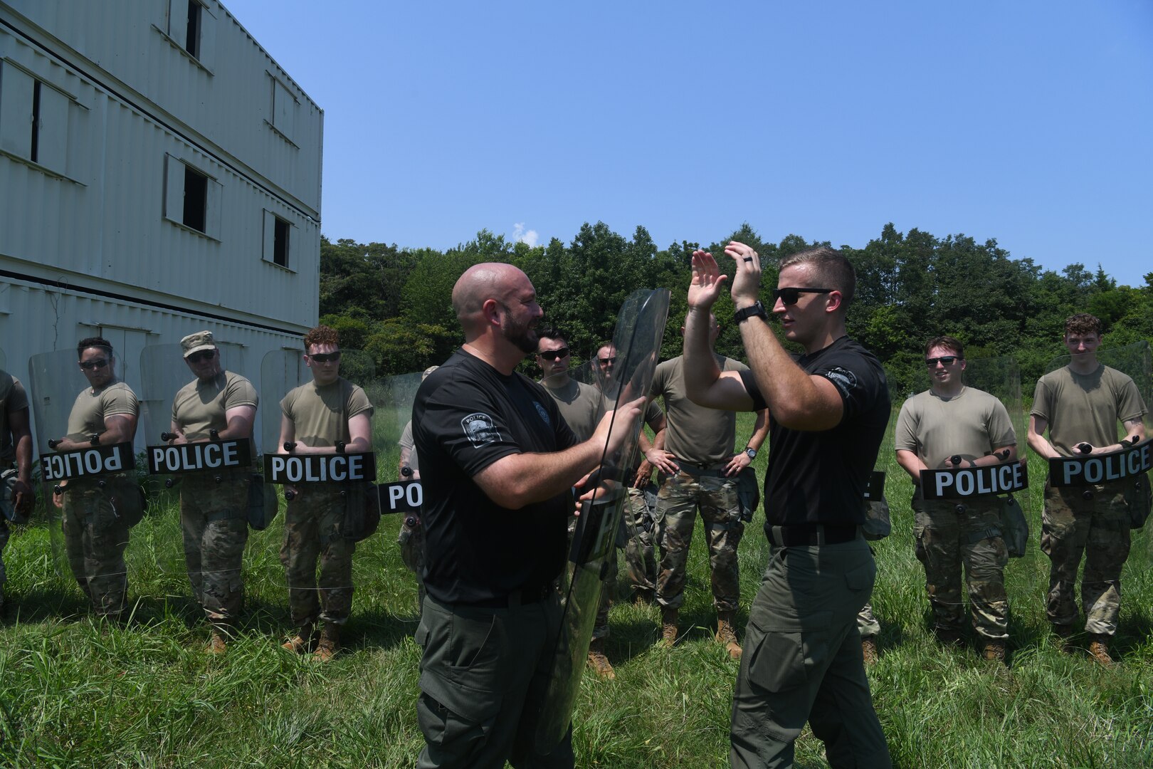 Two police officers demonstrating techniques to line of Airmen holding police shields behind them.