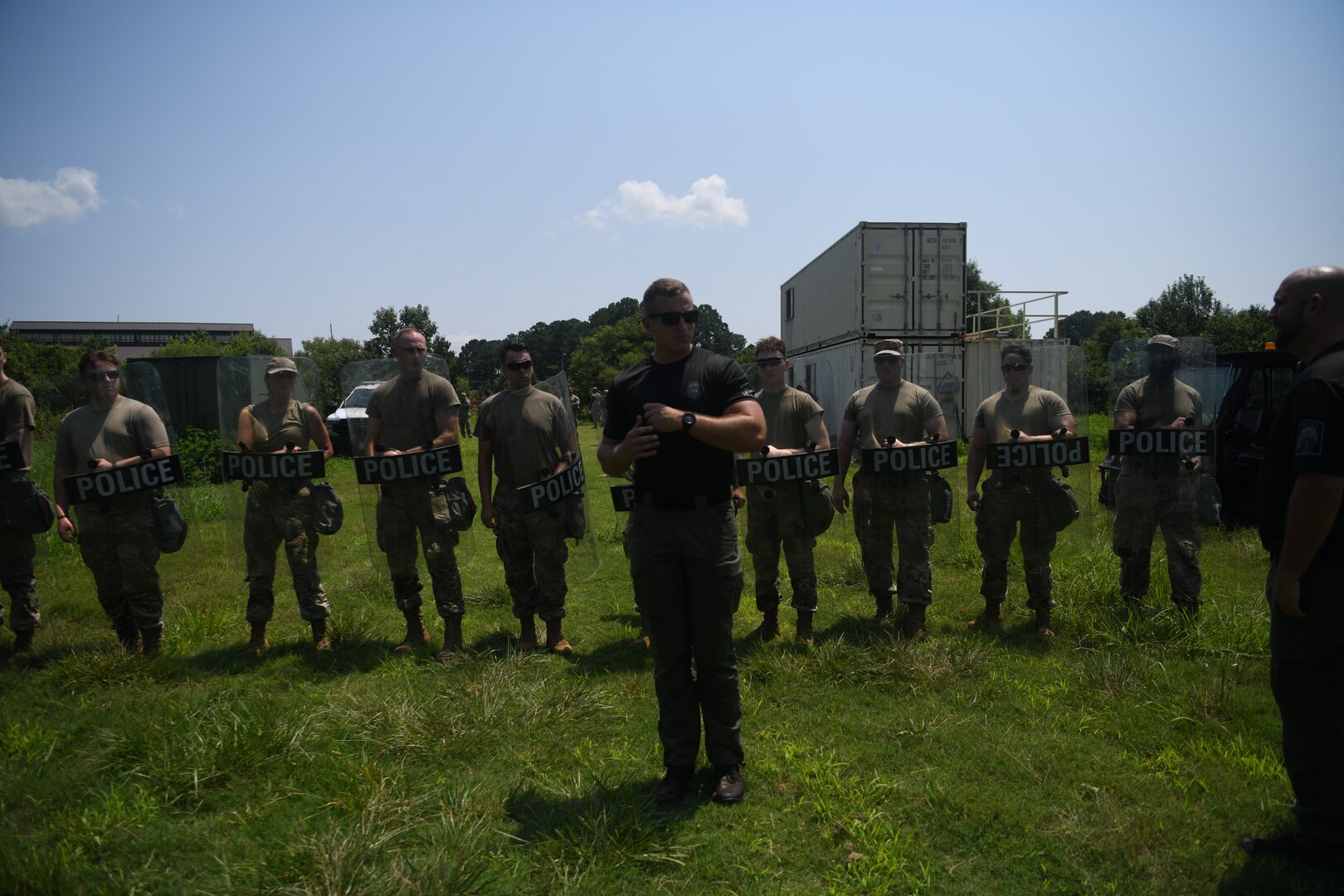 Police officer demonstrating techniques to line of Airmen holding police shields behind him.