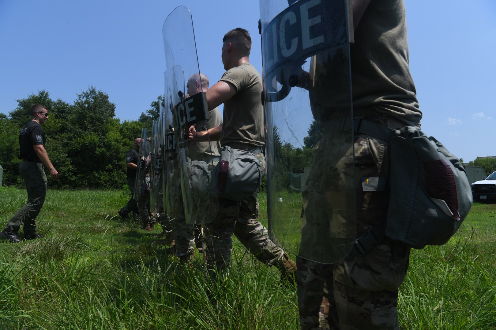 Line of Airmen with police shields walking through field during training.