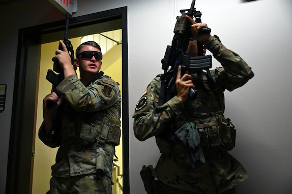 Two service members hold weapons inside a room during training.