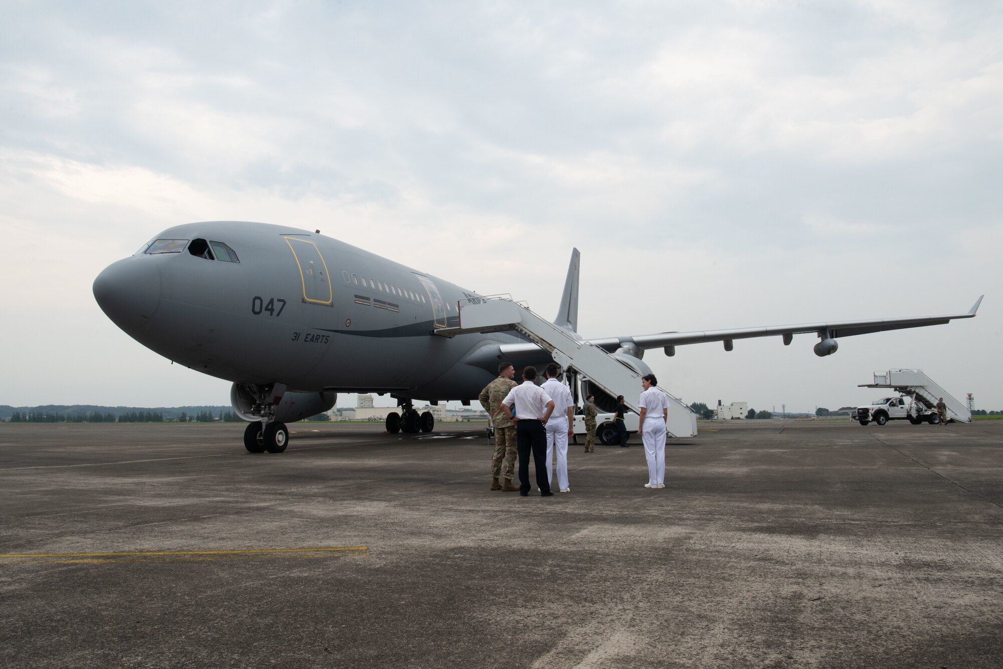 A large airplane stands idle with French and U.S. military members standing in front.