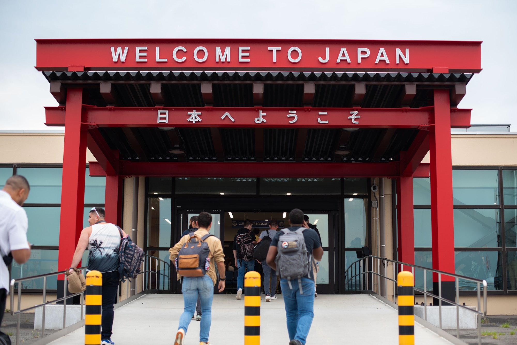 People walk through a large red gate inscribed with "Welcome to Japan" before entering an airport terminal.