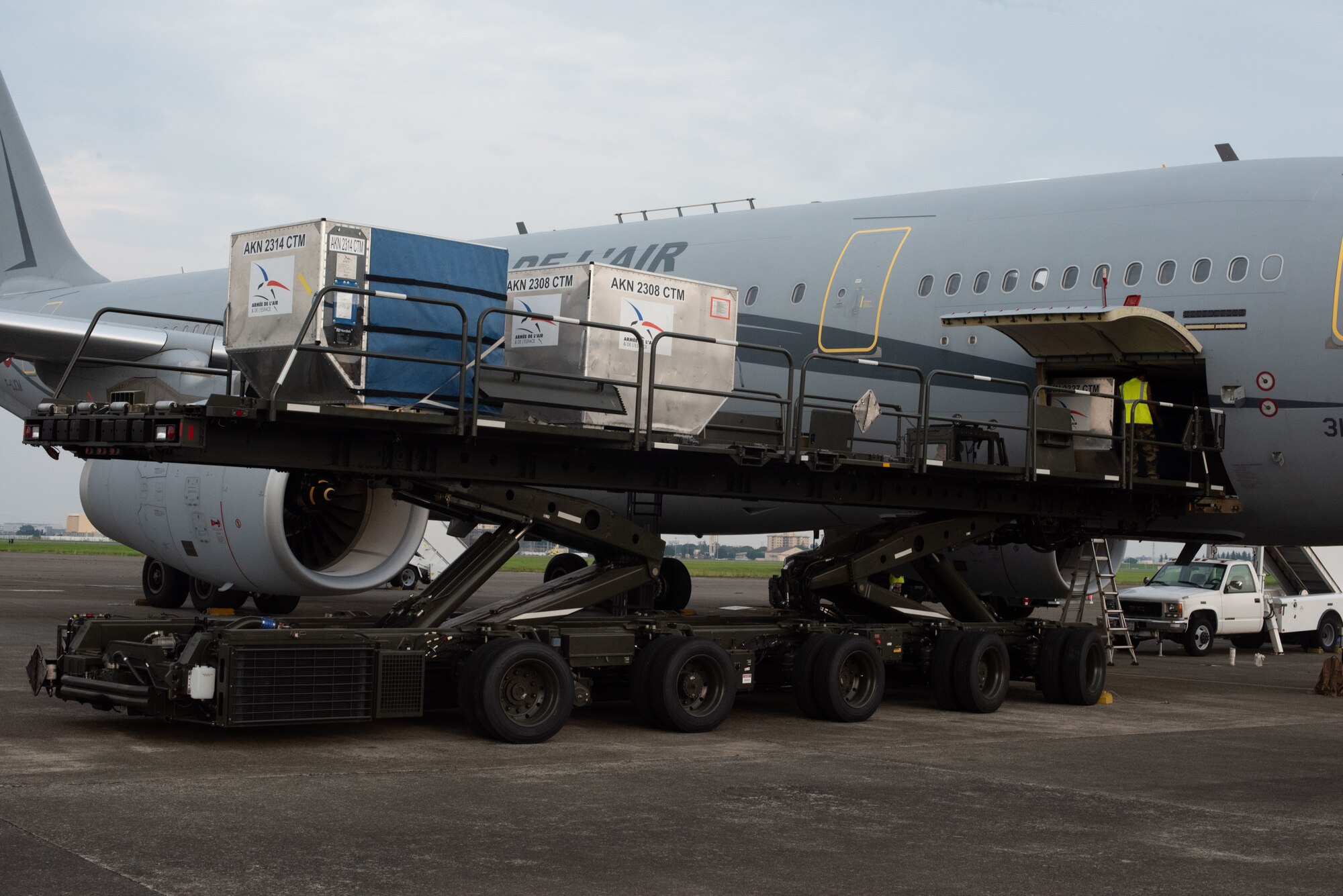 A large platform vehicle holding cargo is raised up against a large airplane.