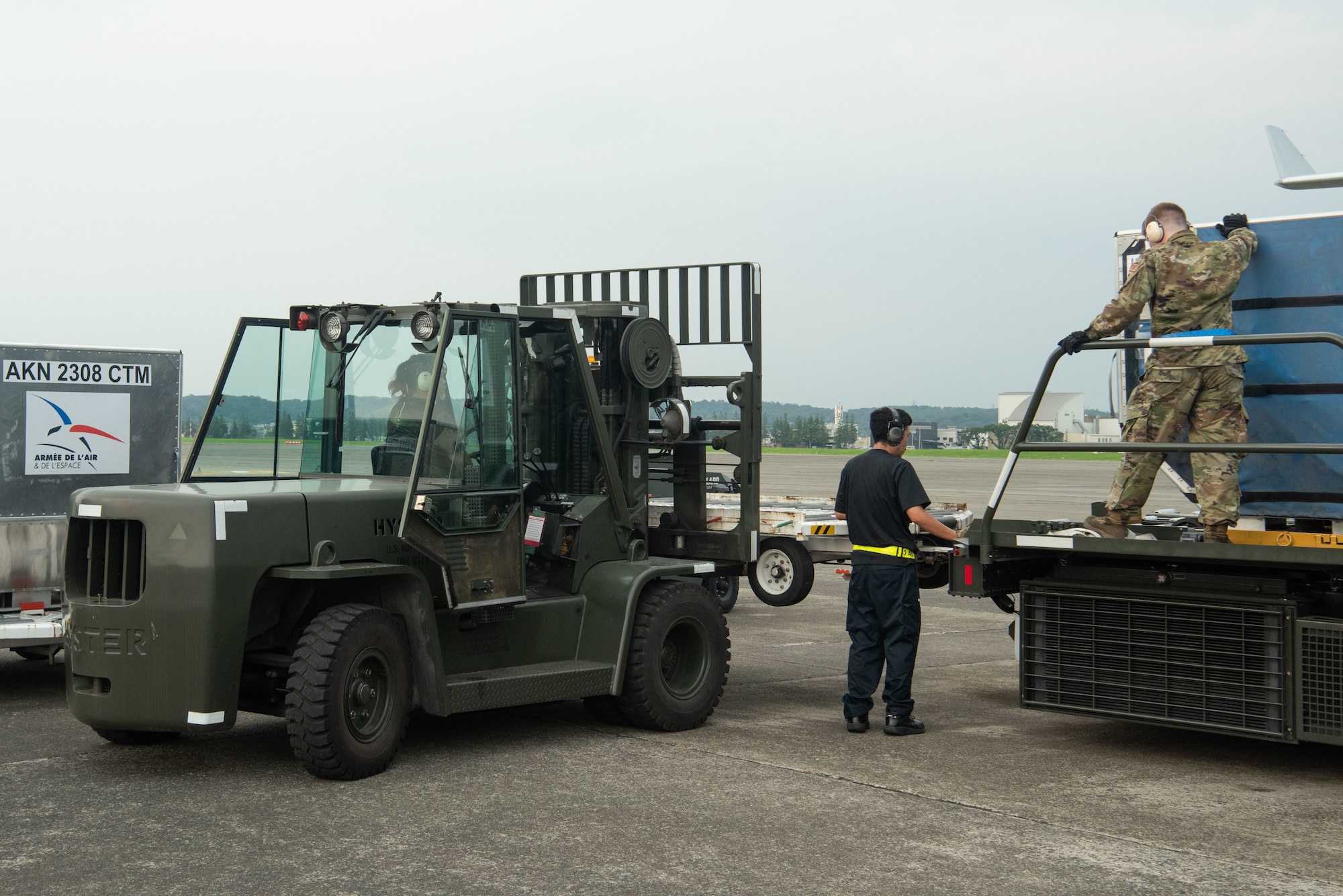 Contractors and a servicemember load a container onto a forklift from a large vehicle.